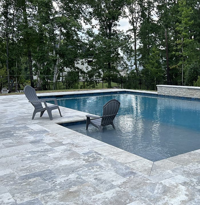 a rectangular concrete pool with patio and lounge chairs