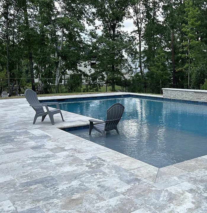 a rectangular concrete pool with patio and lounge chairs